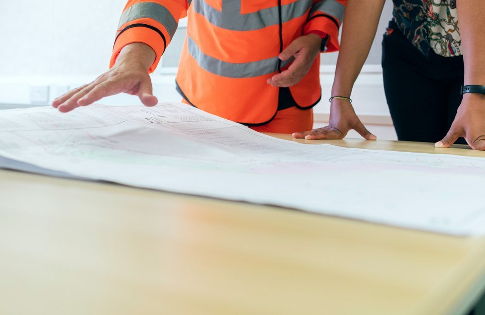 Two people reviewing a large rolled-out construction plan on a table, hands pointing to details