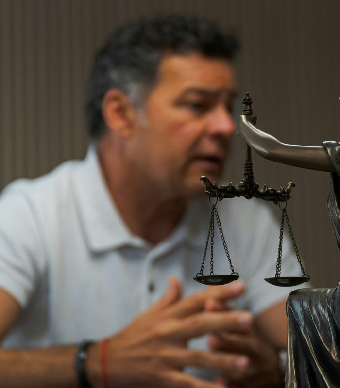 A small statue of Lady Justice holding scales, with a person seated in soft focus in the background