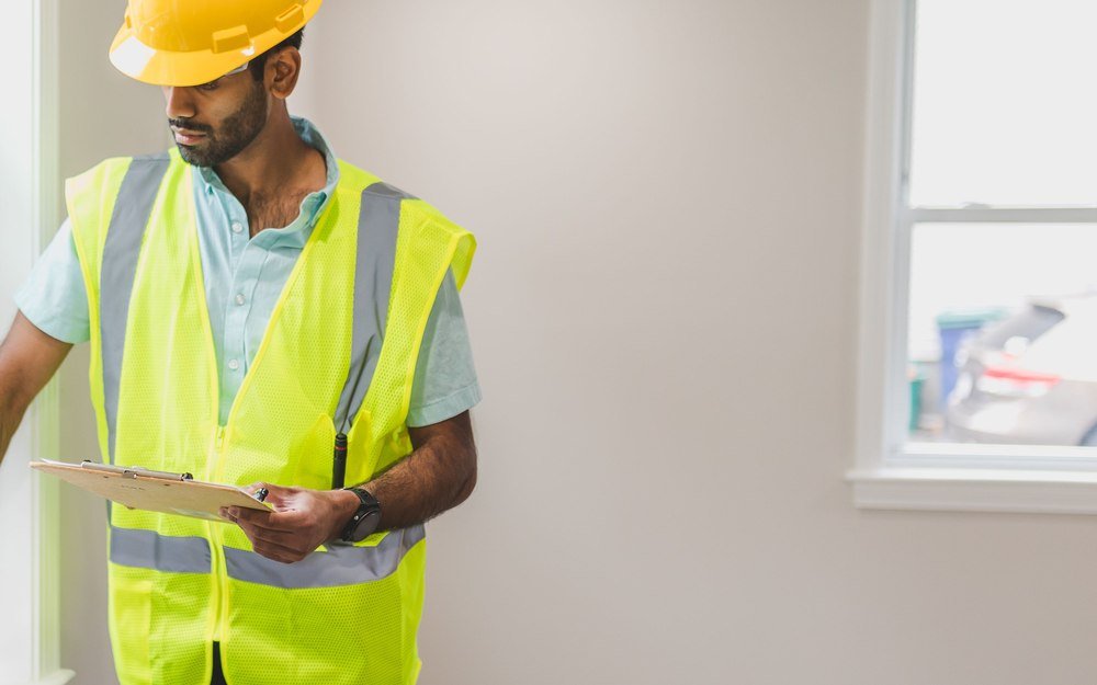 A building inspector with a clipboard examining a newly installed window inside a home under construction