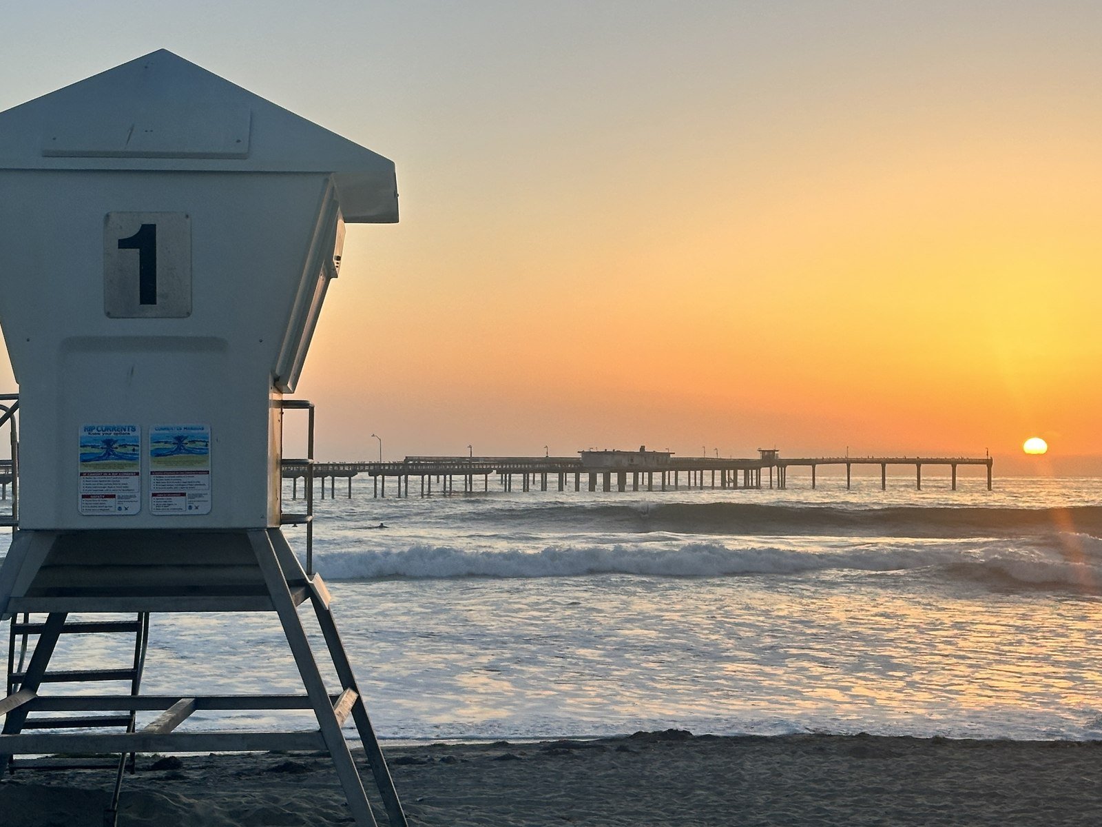 California coastline at sunset with lifeguard tower and pier